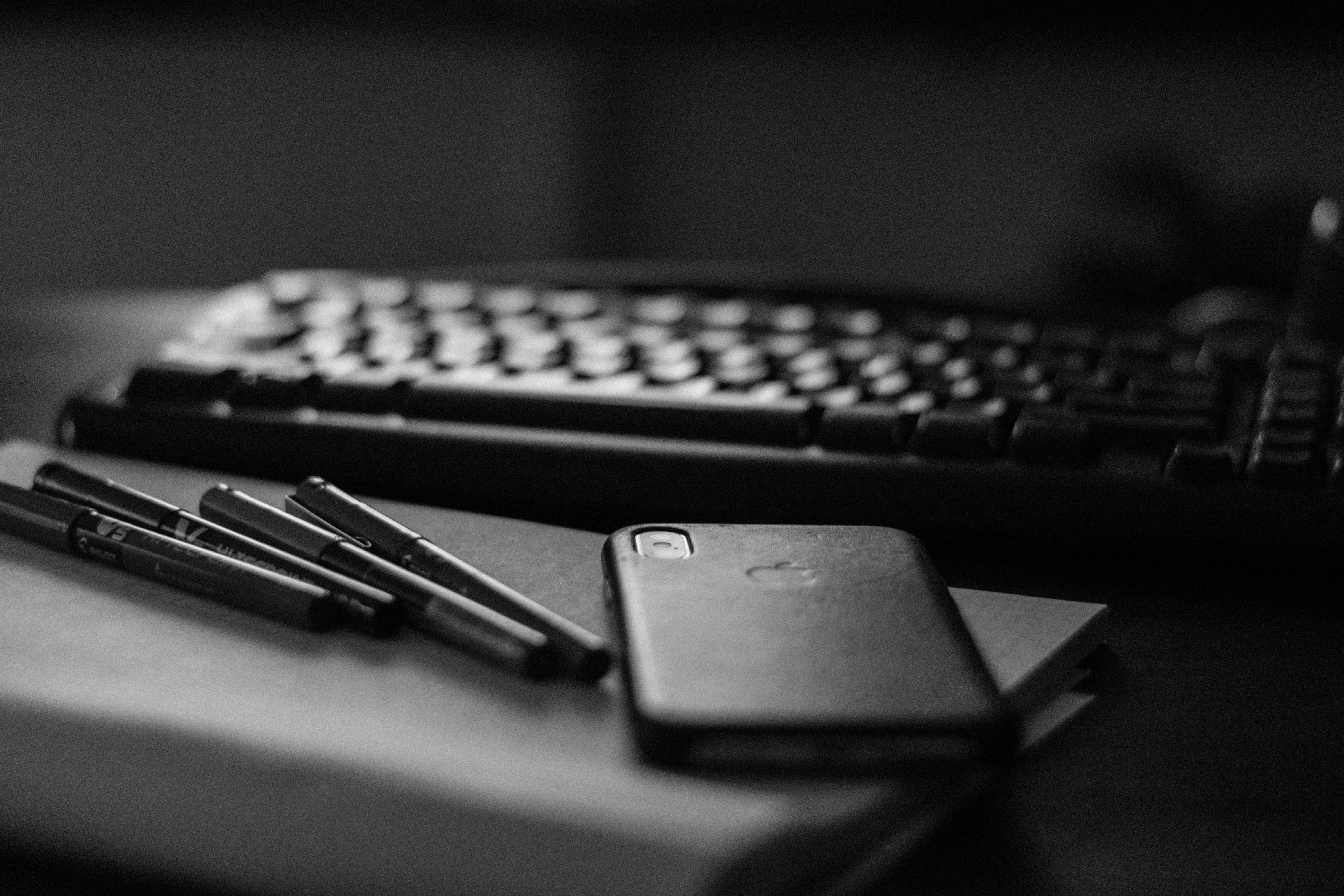 Black iPhone, pens, book and keyboard